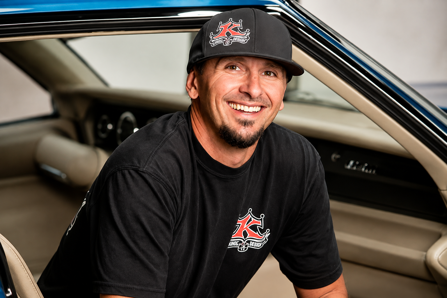 Smiling man wearing a black cap and T-shirt seated inside a classic car