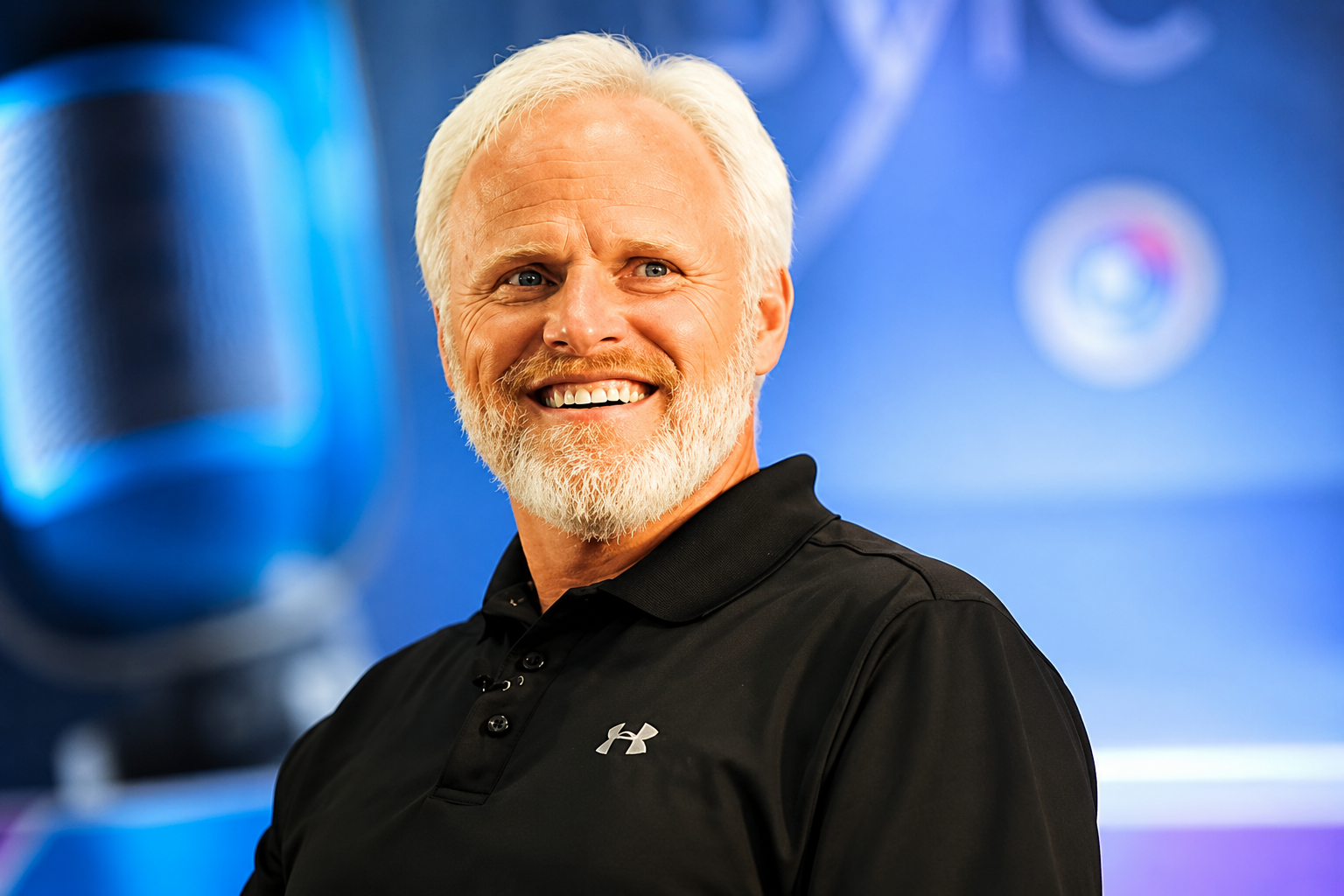 Dan Mohler smiling in a black polo shirt during a studio appearance