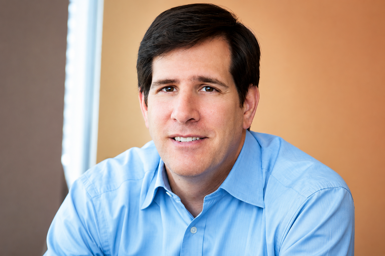 Neal Aronson smiling in a light blue shirt in a professional portrait