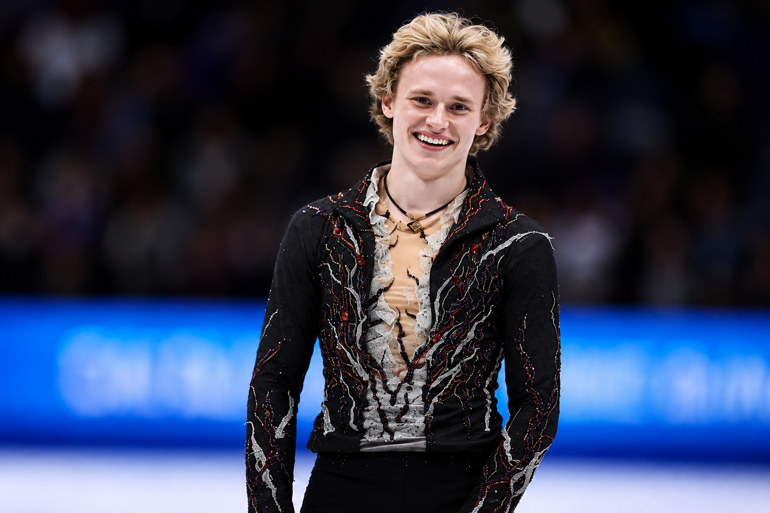 Ilia Malinin smiling in a black and silver figure skating costume