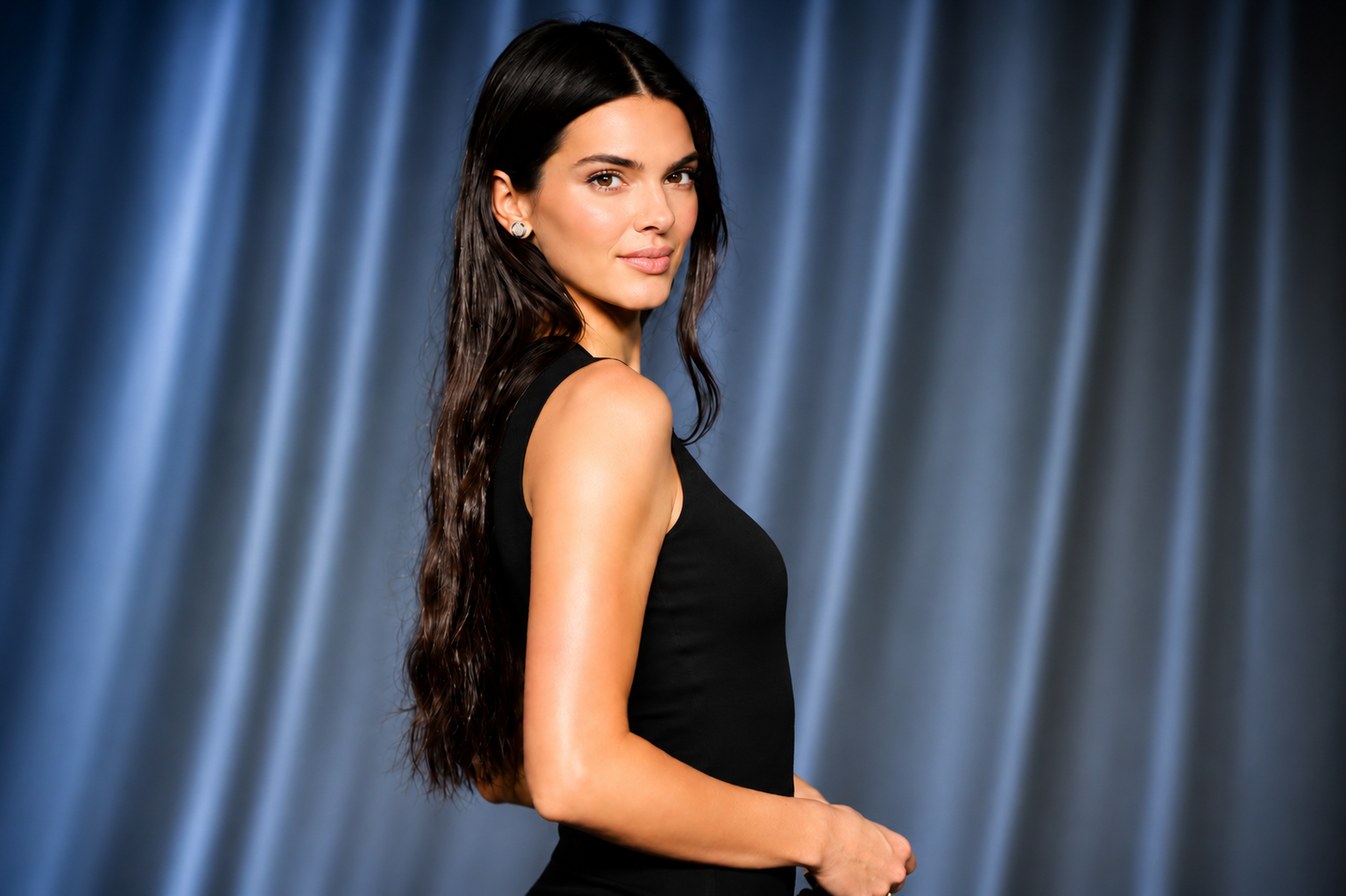 Kendall Jenner posing in a black sleeveless outfit against a blue studio backdrop