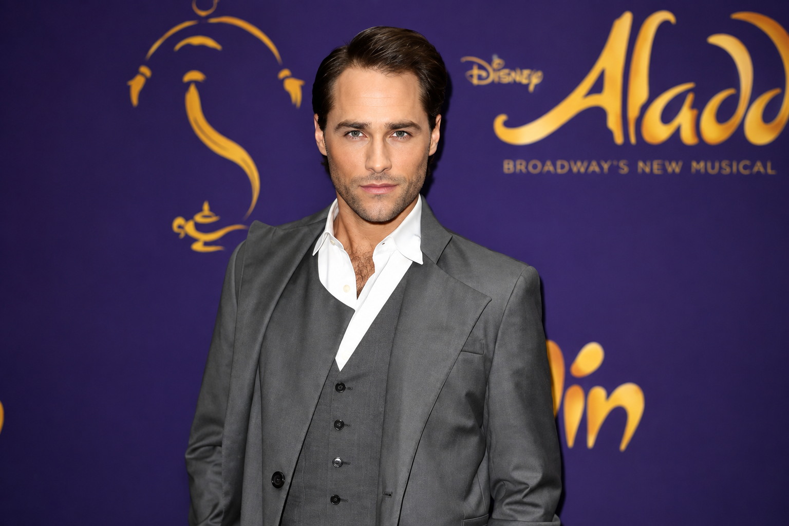 Josh Strickland posing in a gray suit at a Disney Aladdin Broadway event