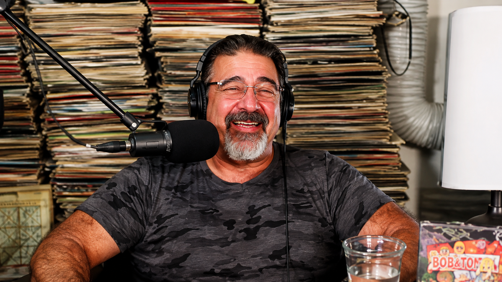 Vinnie DiMartino laughing during a podcast interview, wearing headphones in front of a wall of vinyl records