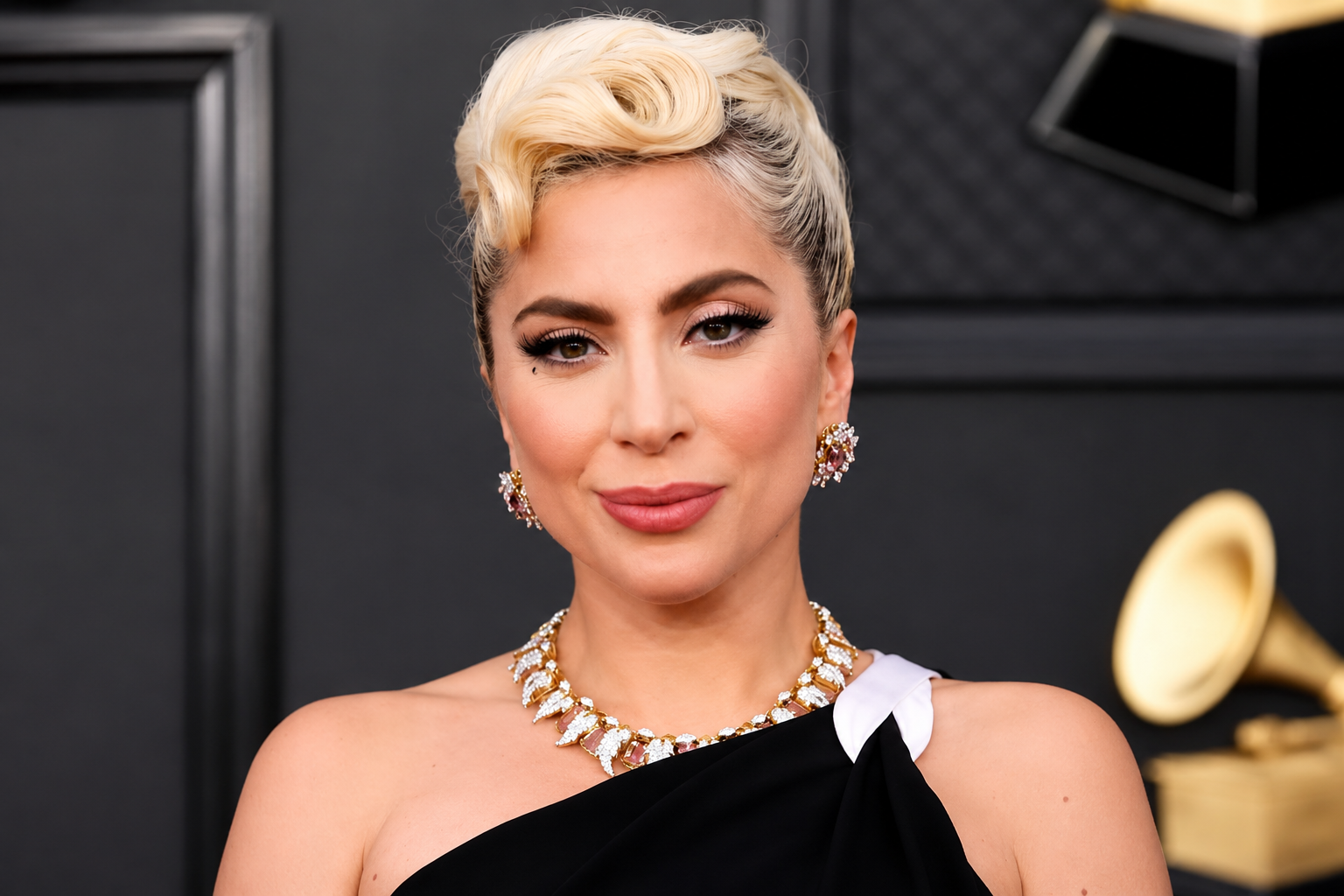 Lady Gaga wearing a black one-shoulder gown and statement jewelry at an awards event