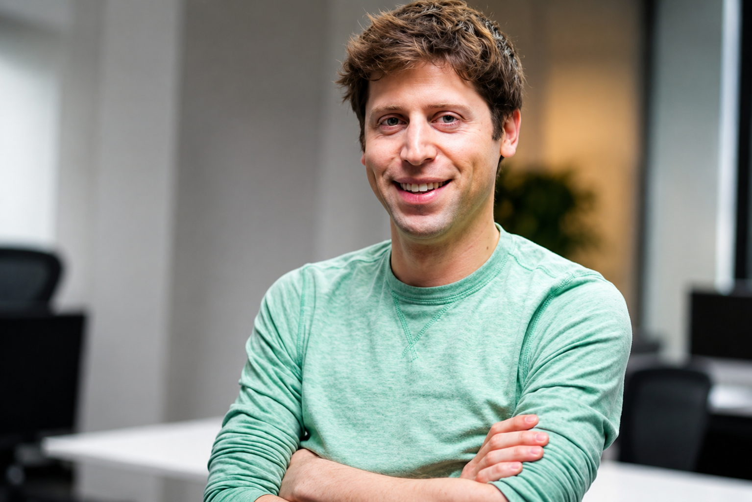Sam Altman smiling while seated in an office wearing a light green shirt