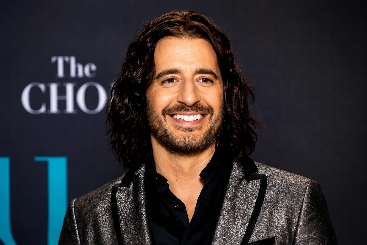 Jonathan Roumie net worth 2026 – smiling in a silver-gray blazer and black shirt