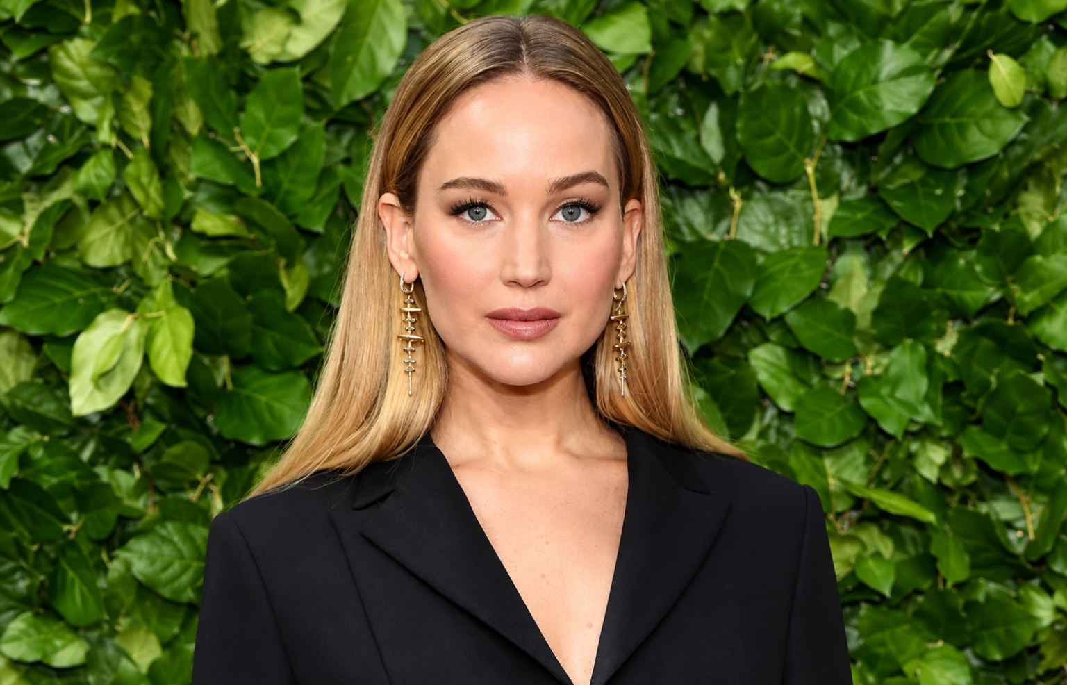 Jennifer Lawrence net worth 2026 – posing in a black blazer with a green leafy background