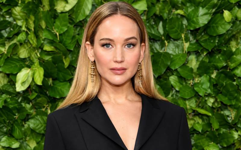 Jennifer Lawrence net worth 2026 – posing in a black blazer with a green leafy background