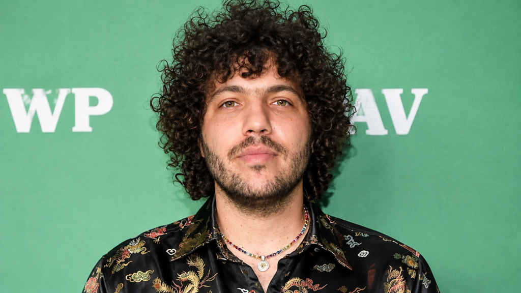 Benny Blanco net worth 2026 – wearing a patterned black shirt and necklaces at a public event