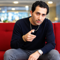 Maksud Agadjani sitting on a red sofa in a black sweater