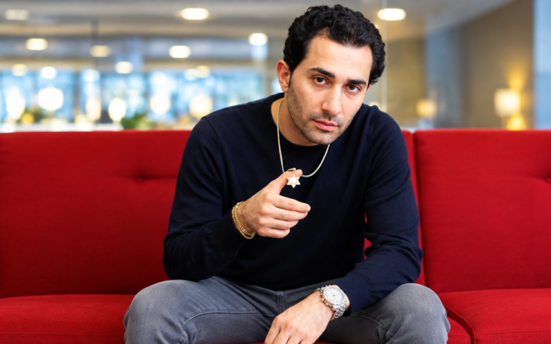 Maksud Agadjani sitting on a red sofa in a black sweater