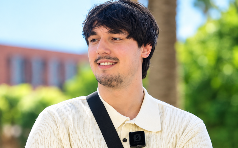 Bryce Hall smiling outdoors in a cream knit polo shirt with a black crossbody strap