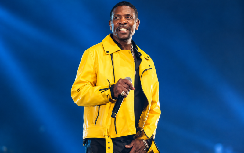 Keith Sweat wearing a yellow jacket and holding a microphone during a live performance.
