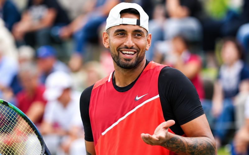 Nick Kyrgios smiling on a tennis court while holding a racket
