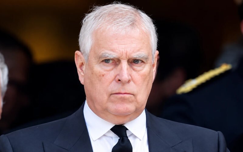 Prince Andrew wearing a dark suit and black tie at a formal event