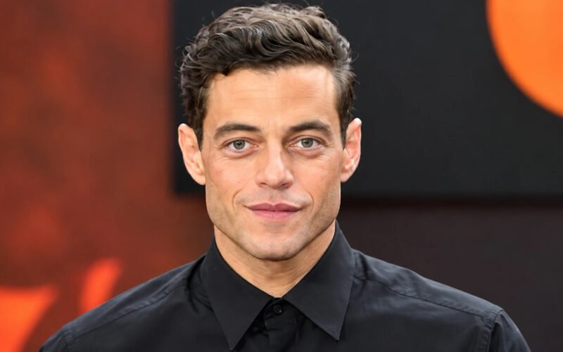 Rami Malek posing in a black shirt at an event