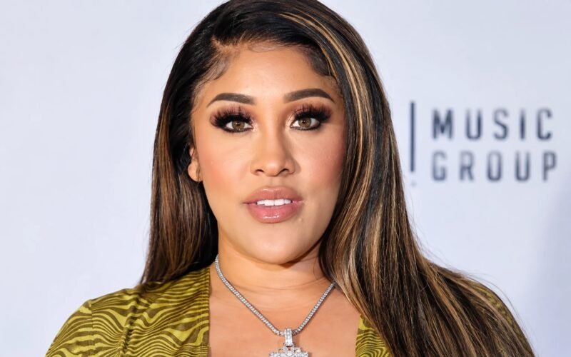Natalie Nunn with long highlighted hair and a silver pendant necklace at a music group event
